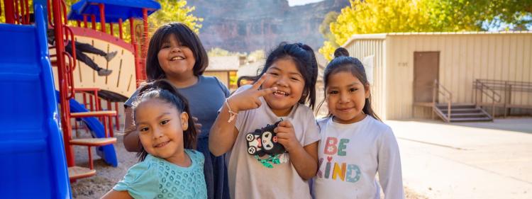 Four Havasupai Elementary School students smile for a photo in front of a colorful playground at the Grand Canyon in Arizona.